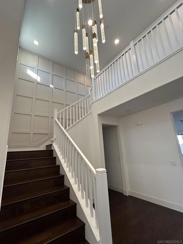 staircase featuring wood-type flooring, a notable chandelier, and a high ceiling