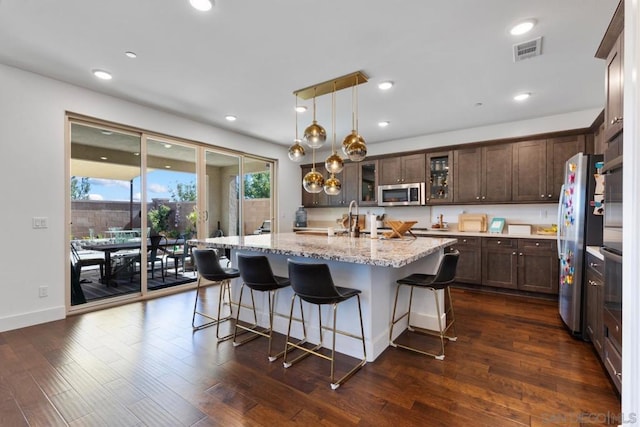 kitchen with a center island with sink, pendant lighting, dark wood-type flooring, and appliances with stainless steel finishes