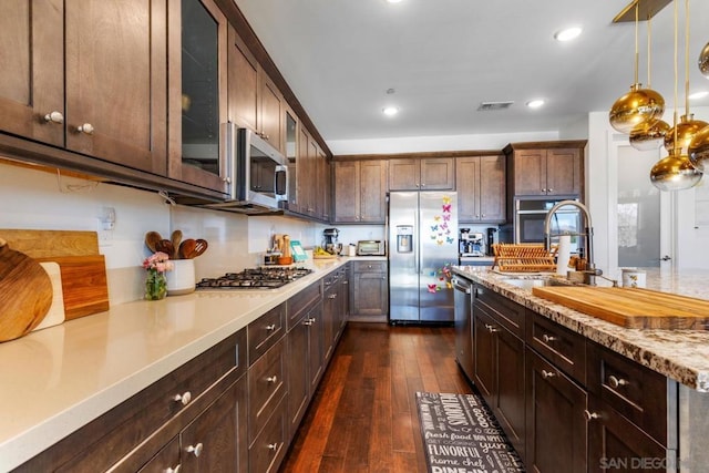 kitchen with pendant lighting, sink, dark hardwood / wood-style floors, appliances with stainless steel finishes, and dark brown cabinetry