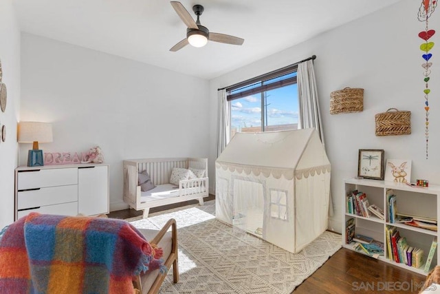 bedroom with a nursery area, light hardwood / wood-style flooring, and ceiling fan