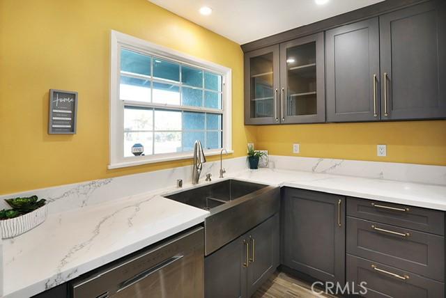8121 San Mateo Cir, Buena Park, CA 90620 - kitchen featuring light wood-type flooring, light stone counters, stainless steel dishwasher, dark brown cabinets, and sink