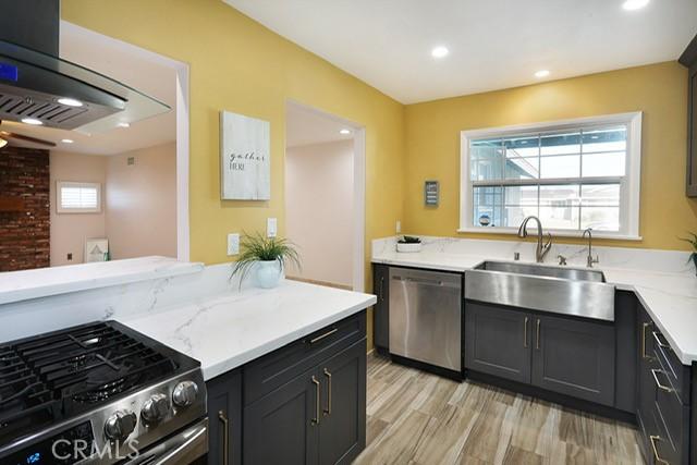 8121 San Mateo Cir, Buena Park, CA 90620 - kitchen with light stone counters, stainless steel appliances, sink, light hardwood / wood-style floors, and range hood