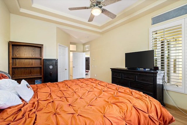 bedroom with light wood-type flooring, a raised ceiling, and ceiling fan