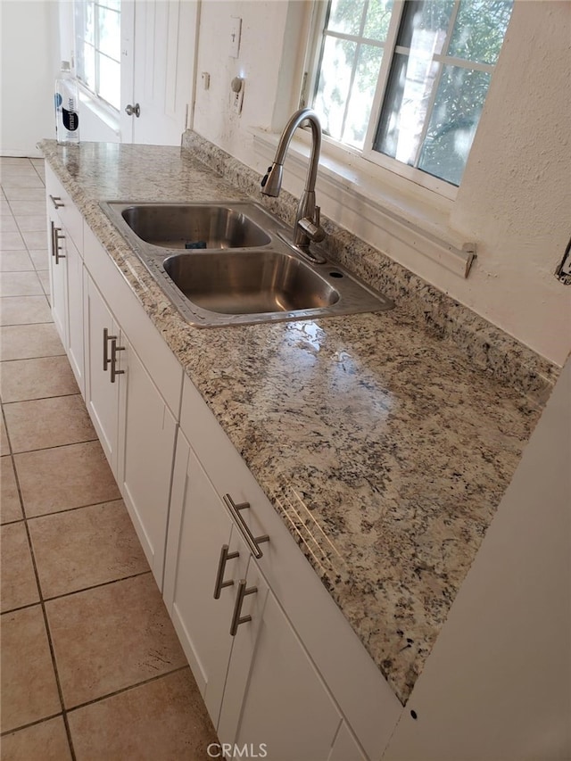 kitchen featuring light tile patterned floors, light stone counters, white cabinetry, and sink