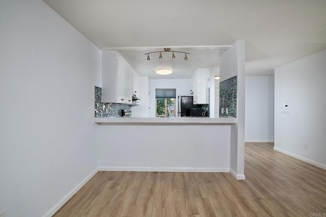 kitchen with tasteful backsplash, kitchen peninsula, white cabinetry, and light hardwood / wood-style flooring