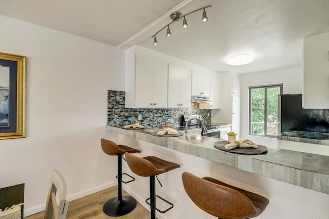 kitchen featuring stainless steel range with electric cooktop, light hardwood / wood-style flooring, decorative backsplash, a kitchen bar, and white cabinetry