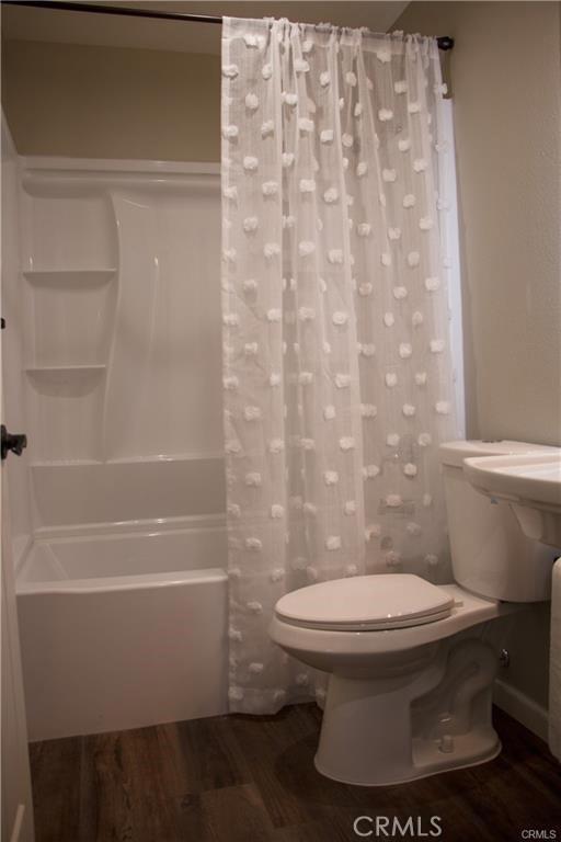 bathroom with hardwood / wood-style flooring, toilet, and shower / bath combo with shower curtain