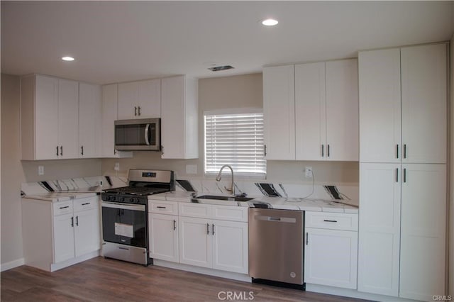 kitchen with light stone countertops, sink, dark wood-type flooring, white cabinets, and appliances with stainless steel finishes