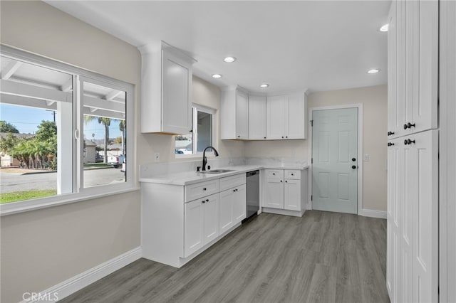 kitchen with white cabinets, light hardwood / wood-style flooring, stainless steel dishwasher, and sink