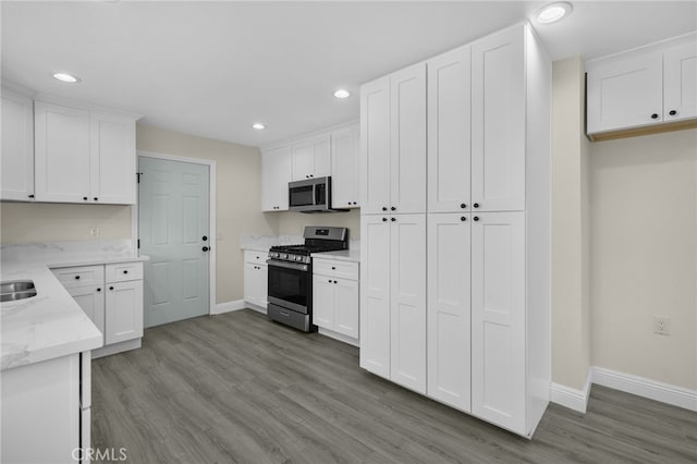 kitchen featuring light stone counters, white cabinets, light wood-type flooring, and appliances with stainless steel finishes