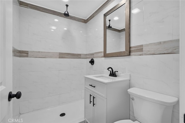 bathroom featuring a tile shower, vanity, toilet, and tile walls