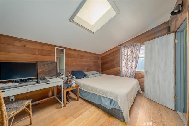 bedroom featuring lofted ceiling with skylight, wood-type flooring, and wooden walls