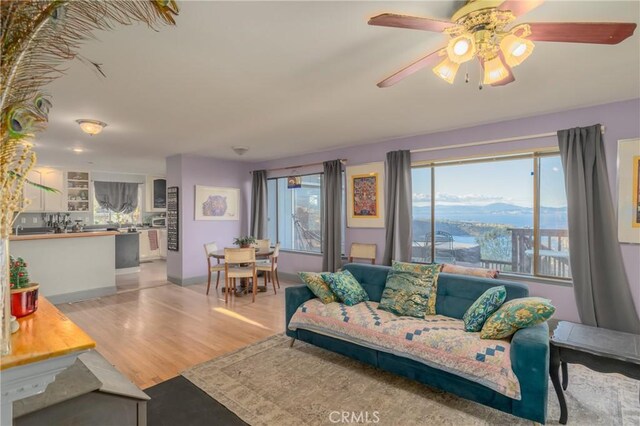 living room with light wood-type flooring, ceiling fan, a mountain view, and plenty of natural light