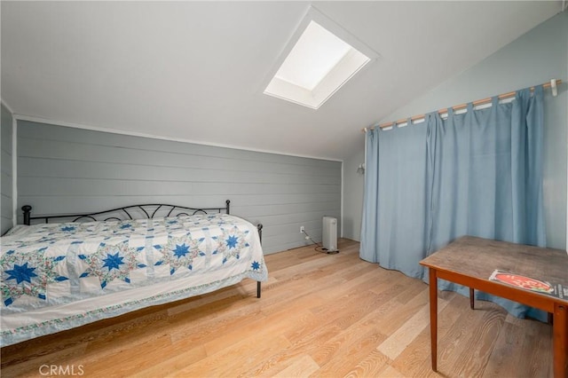 bedroom featuring wooden walls, vaulted ceiling with skylight, and light hardwood / wood-style floors