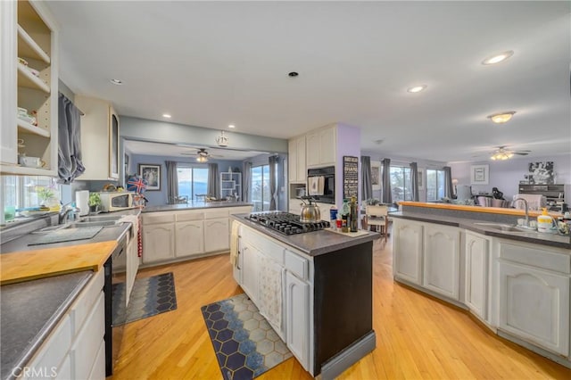 kitchen featuring light wood-type flooring, kitchen peninsula, black appliances, sink, and white cabinets