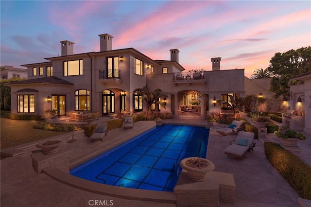 back house at dusk featuring a patio and a balcony