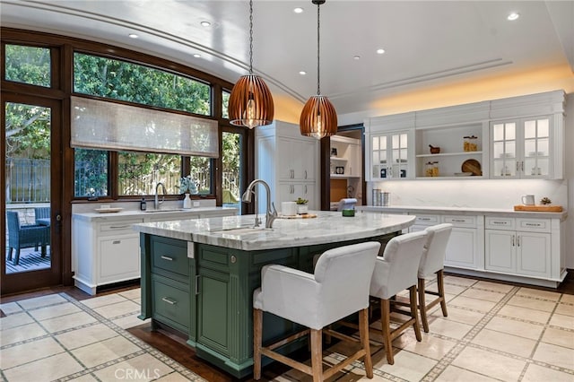 kitchen featuring light stone counters, white cabinetry, a kitchen island with sink, and green cabinetry