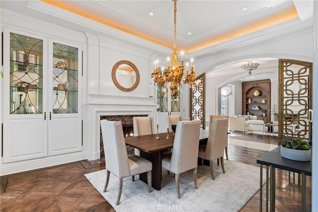 dining area featuring dark parquet flooring, french doors, a raised ceiling, a high end fireplace, and a notable chandelier