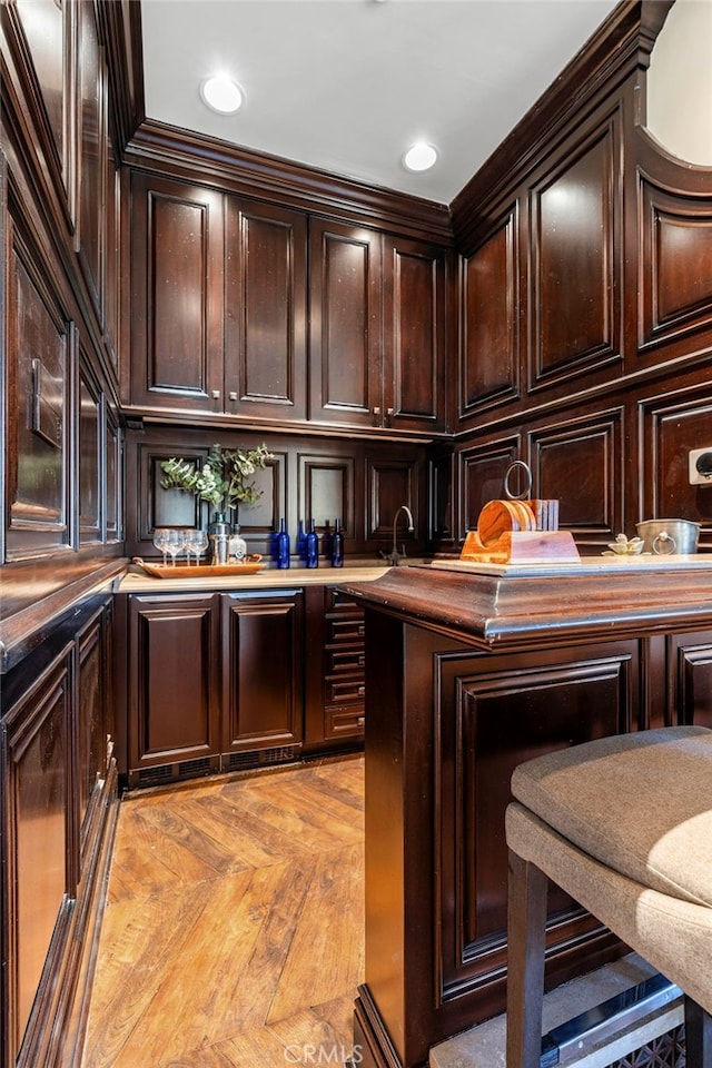 bar with dark brown cabinetry, light parquet floors, and ornamental molding