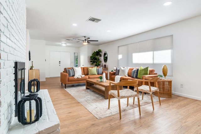 living room with ceiling fan, light hardwood / wood-style floors, and a brick fireplace