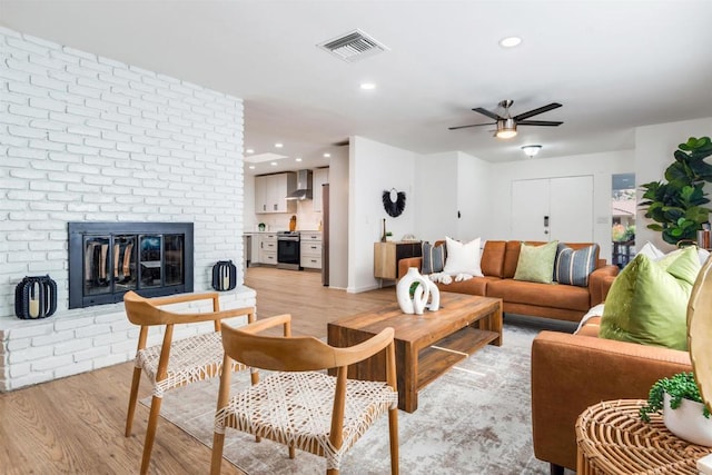 living room with ceiling fan, light hardwood / wood-style floors, and a brick fireplace