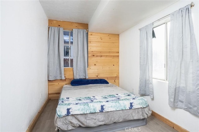 bedroom featuring multiple windows, wooden walls, and wood-type flooring