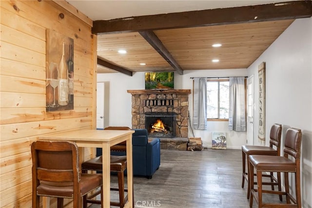 interior space with wood ceiling, dark wood-type flooring, beamed ceiling, a stone fireplace, and wood walls