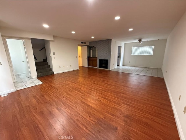 unfurnished living room featuring a brick fireplace, light hardwood / wood-style flooring, and ceiling fan