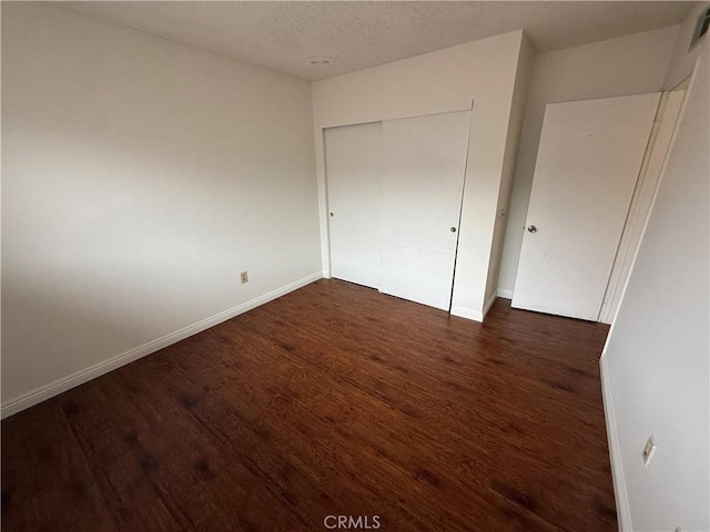 unfurnished bedroom with a textured ceiling, a closet, and dark hardwood / wood-style floors