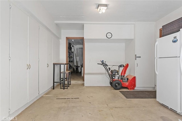 interior space featuring unfinished concrete floors, freestanding refrigerator, and white cabinetry