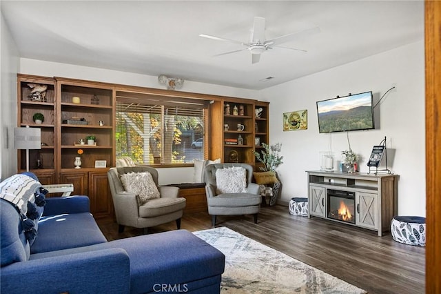 living area with a glass covered fireplace, dark wood finished floors, and a ceiling fan