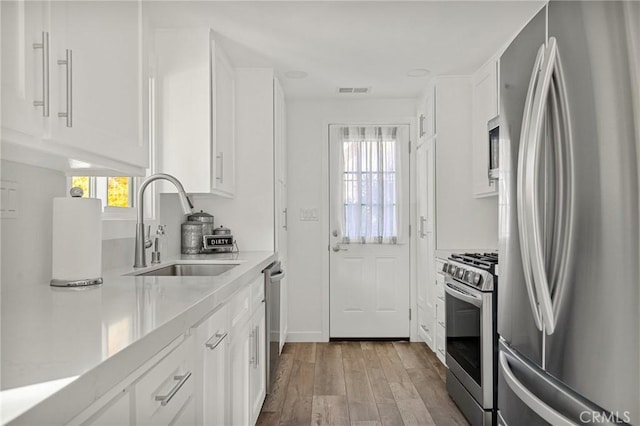 kitchen with a sink, stainless steel appliances, light countertops, and white cabinetry