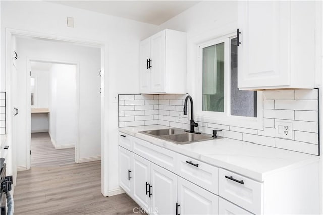 kitchen featuring sink, light stone countertops, tasteful backsplash, light hardwood / wood-style floors, and white cabinetry