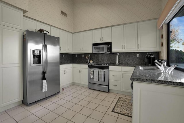 kitchen featuring backsplash, stainless steel appliances, light tile patterned floors, a high ceiling, and white cabinetry