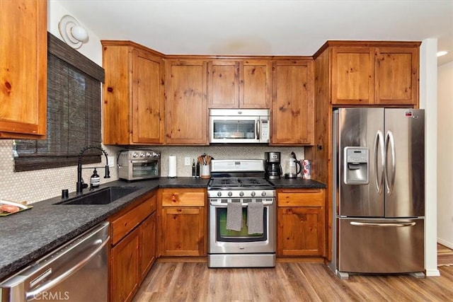 kitchen with backsplash, sink, stainless steel appliances, and light hardwood / wood-style floors