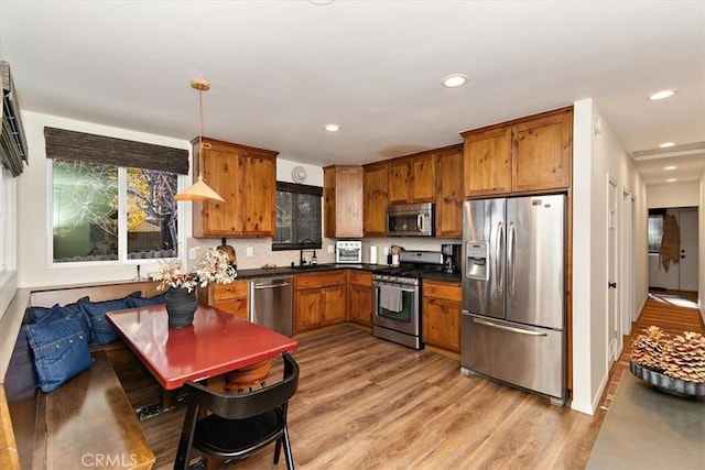 kitchen featuring sink, stainless steel appliances, light hardwood / wood-style flooring, backsplash, and decorative light fixtures