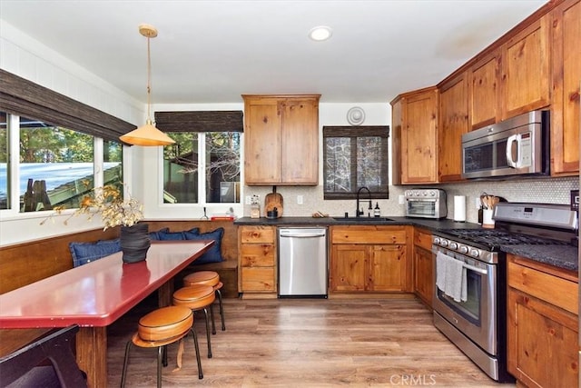 kitchen featuring sink, hanging light fixtures, decorative backsplash, light hardwood / wood-style floors, and stainless steel appliances