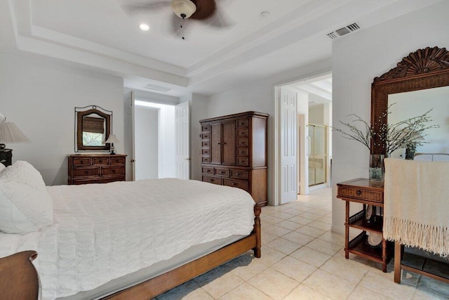 bedroom with ceiling fan, light tile patterned floors, a tray ceiling, and connected bathroom