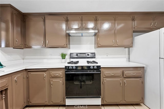 kitchen with range, white refrigerator, light tile patterned floors, and exhaust hood