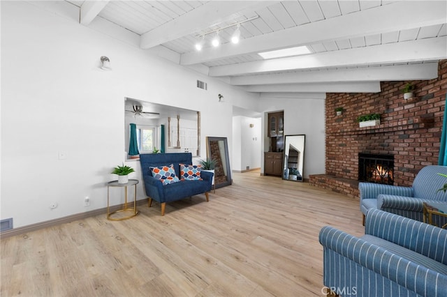 living room featuring hardwood / wood-style floors, track lighting, lofted ceiling with beams, a brick fireplace, and ceiling fan