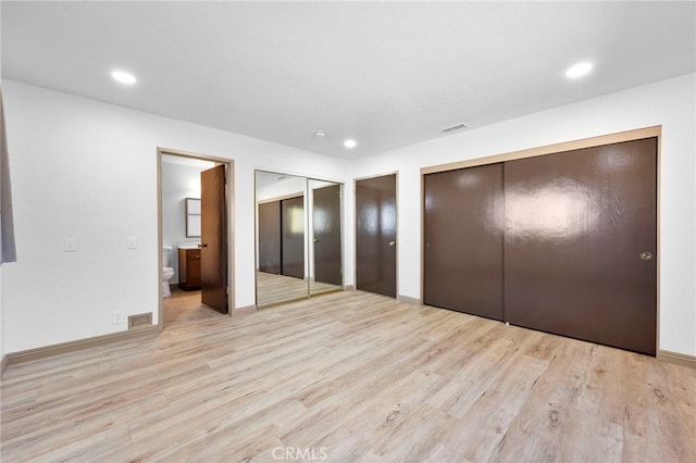 unfurnished bedroom featuring light wood-type flooring, ensuite bathroom, and multiple closets