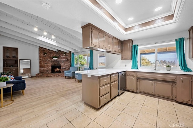 kitchen with dishwasher, sink, a brick fireplace, light hardwood / wood-style flooring, and kitchen peninsula