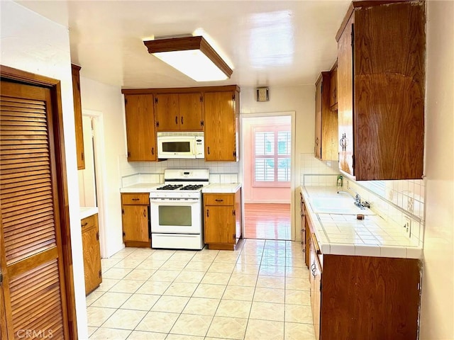 kitchen with sink, white appliances, tile counters, and backsplash