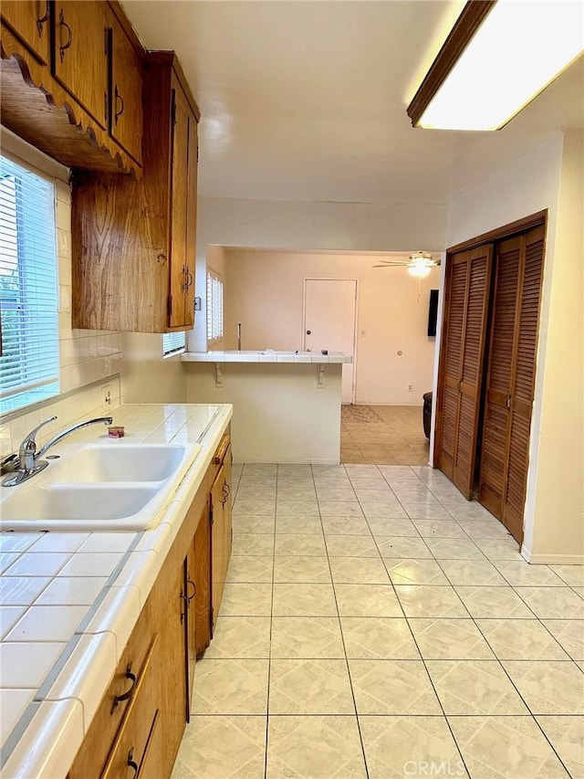 kitchen featuring tile countertops, ceiling fan, light tile patterned floors, and sink