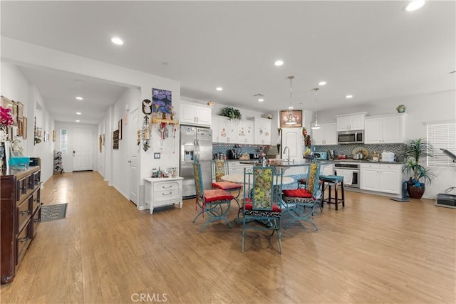 kitchen featuring a center island with sink, decorative backsplash, light wood-type flooring, appliances with stainless steel finishes, and decorative light fixtures