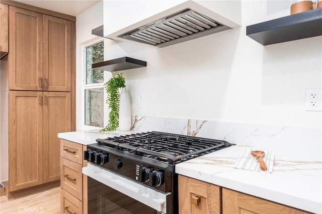 kitchen featuring light stone countertops, stainless steel gas stove, premium range hood, and light hardwood / wood-style flooring