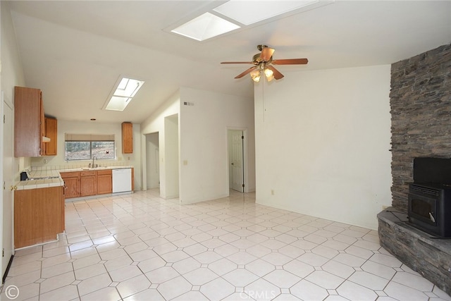 unfurnished living room with ceiling fan, sink, a wood stove, and a skylight