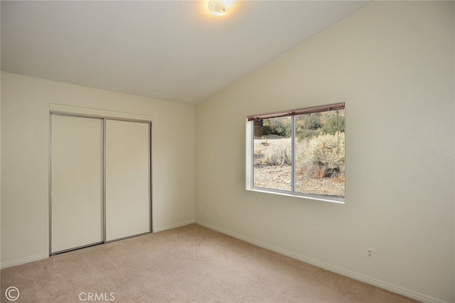 unfurnished bedroom with vaulted ceiling, a closet, and light colored carpet