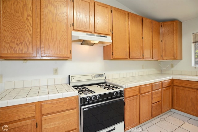 kitchen with light tile patterned flooring, tile countertops, and white gas range