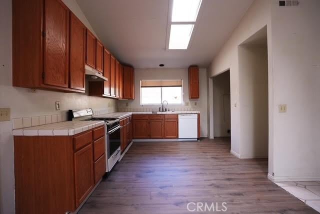 kitchen with tile countertops, sink, light hardwood / wood-style floors, and white appliances